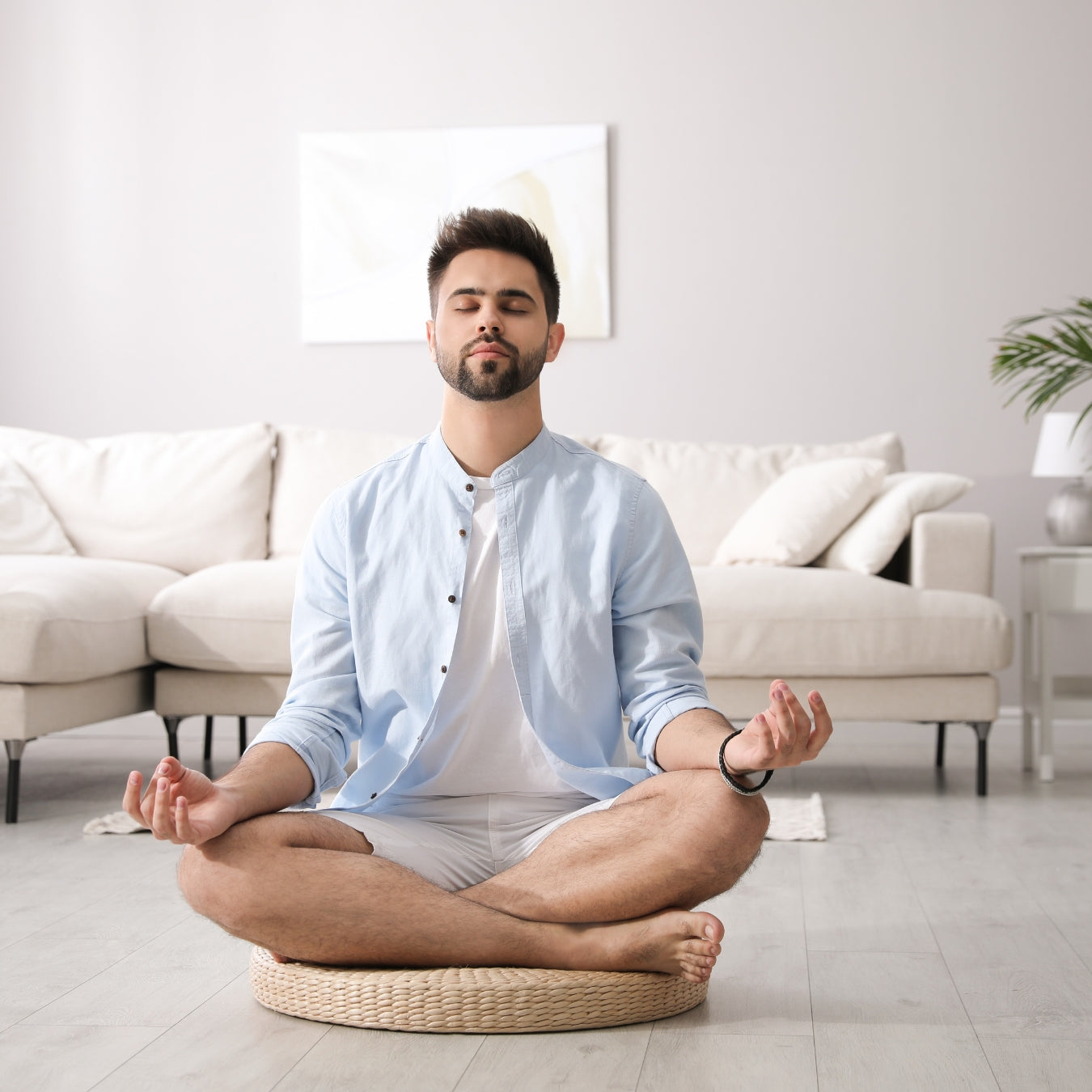 Man meditating on a woven cushion in a modern living room.