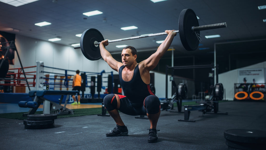 Athletic man performing overhead barbell squat in modern fitness gym