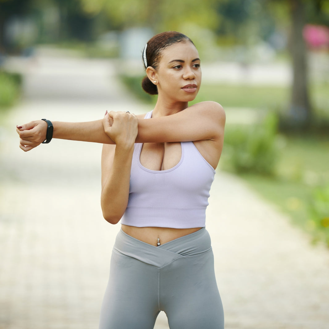 Woman in white tank top stretching arms during outdoor workout session